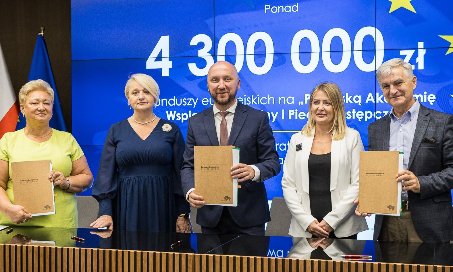 Marszałek Łukasz Prokorym stoi w towarzystwie uczestników konferencji. Trzyma teczkę, z dokumentami dotyczącymi projektu.