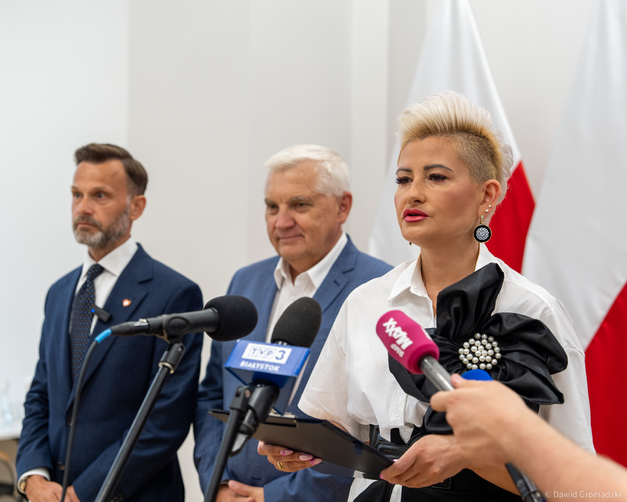 Trzy osoby na konferencji przed mikrofonami.