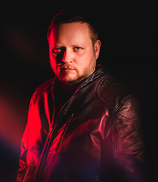 portret mężczyzny w skurzanej czarnej kurtce, lekki zarost na twarzy, oświetlonej czerwonym światłem