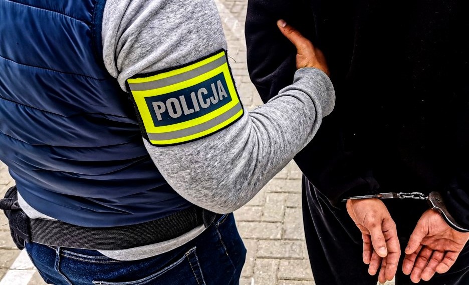 Mężczyzna z założonymi kajdankami, jest prowadzony przez policjanta