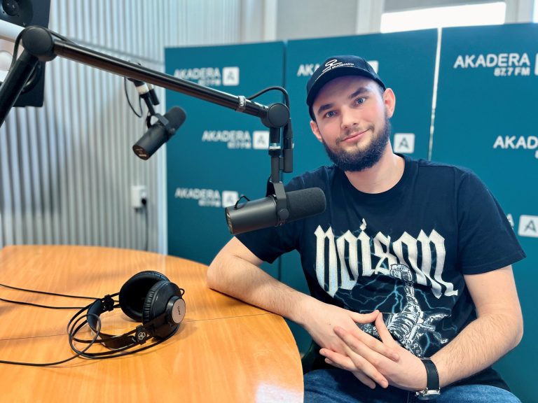 Młody chłopak siedzi przy stole, w czapce i koszulce, ma ciemną brodę