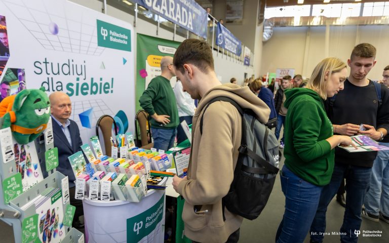 Uczeń stoi przy stoisku promocyjnym uczelni.