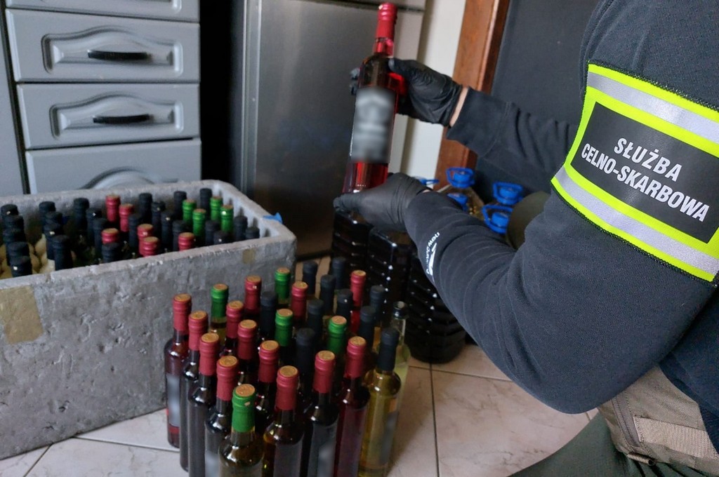 Ręka celnika trzymająca butelkę alkoholu. na podłodze dużo butelek