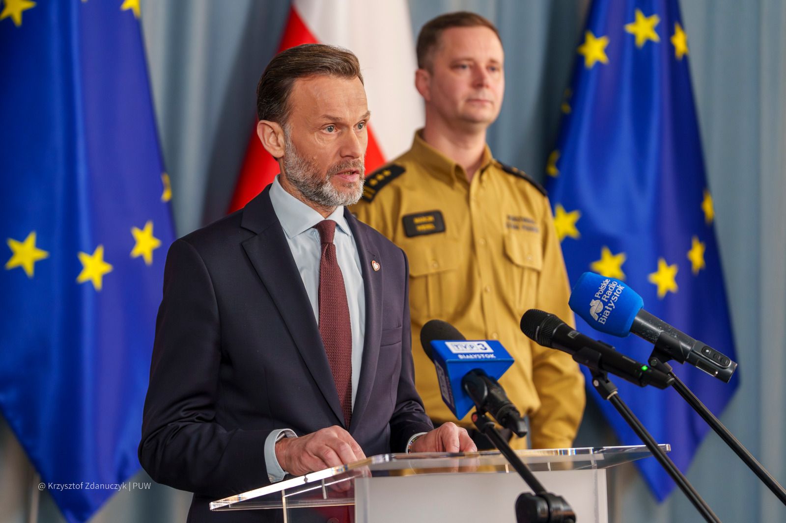 Mężczyzna w garniturze i strażak na konferencji prasowej.