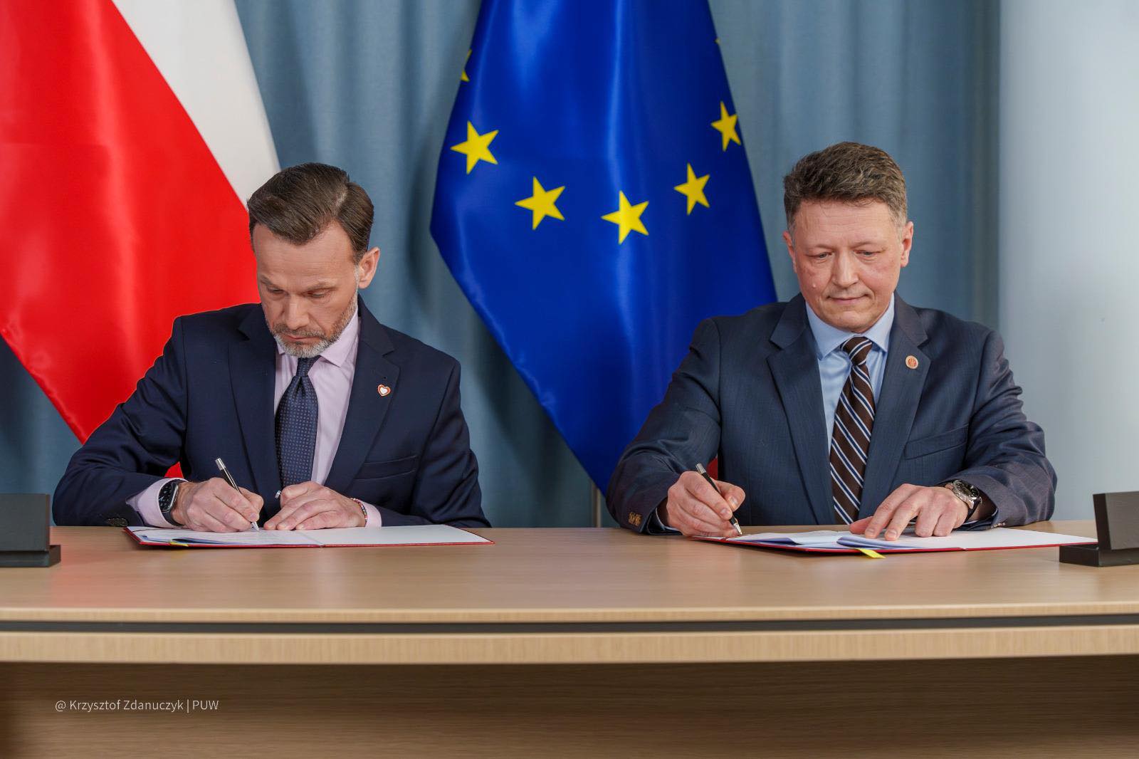 Dwóch mężczyzn w garniturach podpisują umowy.