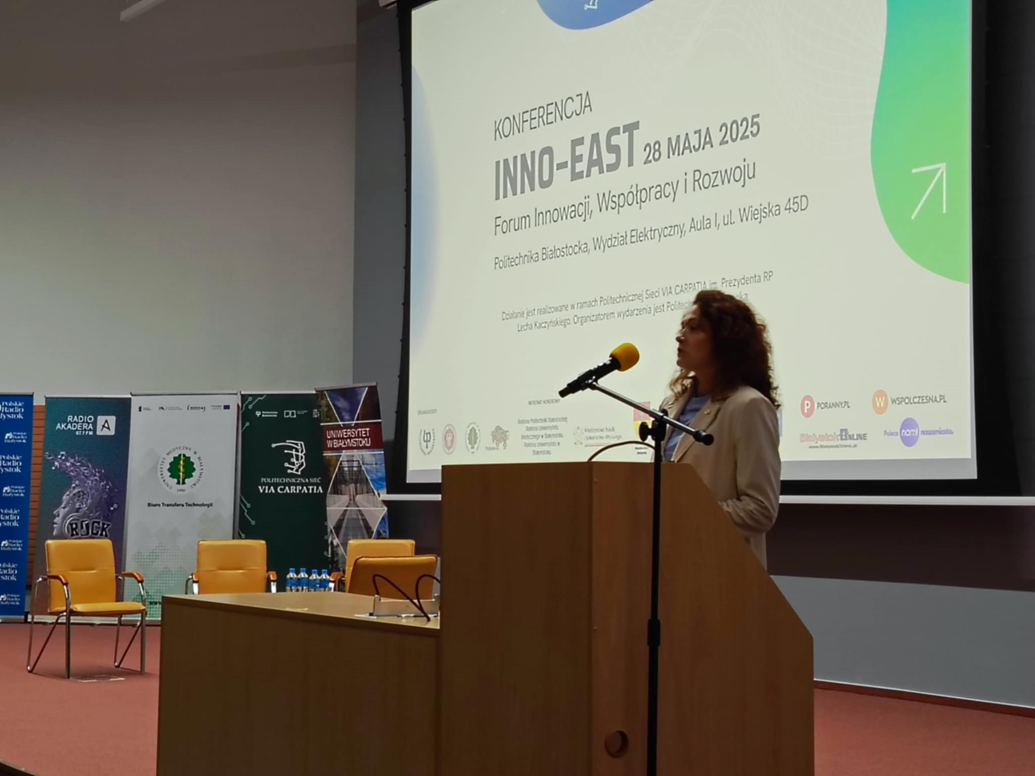 Kobieta na mównicy przemawia na tle wyświetlanego napisu z tematyka konferencji