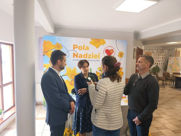 Joanna Czupryńska-Kwiatkowska i Eryk Latocha z Fundacji „Pomóż Im” udzielają wywiadu mediom podczas konferencji prasowej kampanii „Pola Nadziei”. W tle ścianka z logo kampanii i żonkilami.