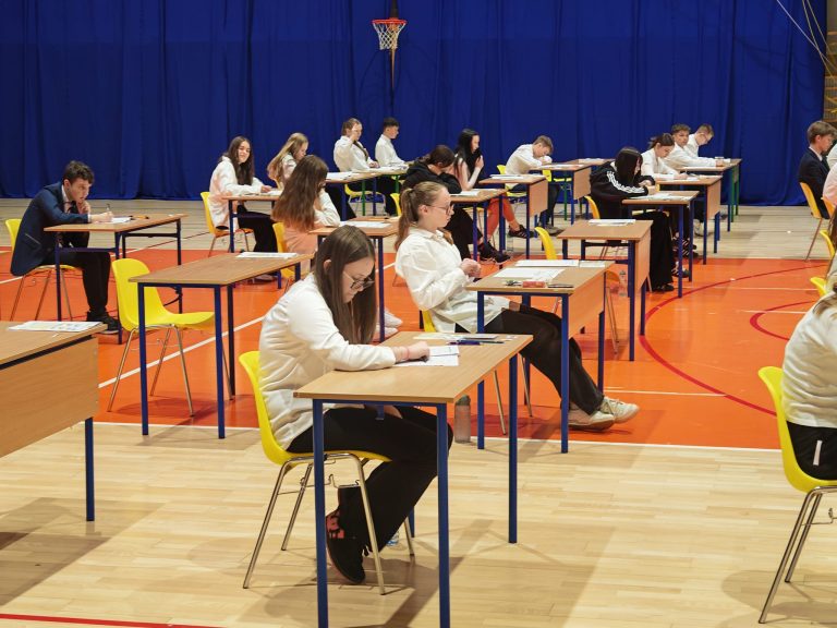 Uczniowie w ławkach na sali gimnastycznej piszą egzamin