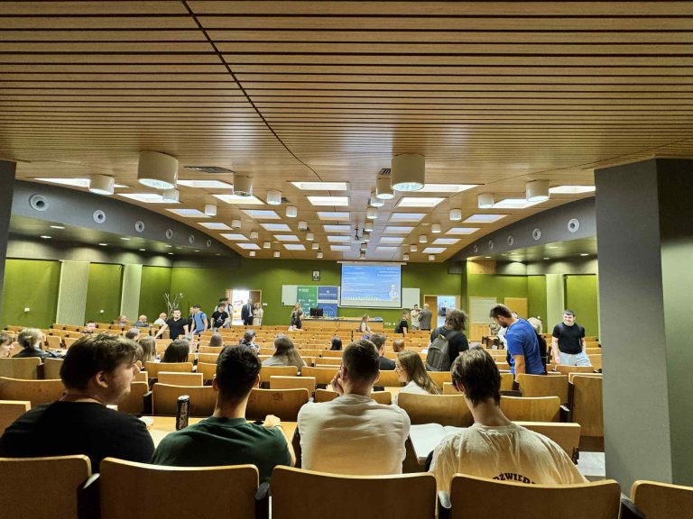 SALA WYKLADOWA SIEDZA STUDENCI W LAWKACH NA DOLE WYSWIETLACZ Z INFORMACJAMI O KONFERENCJI BEZPIECZENSTWO W BUDOWNICTWIE