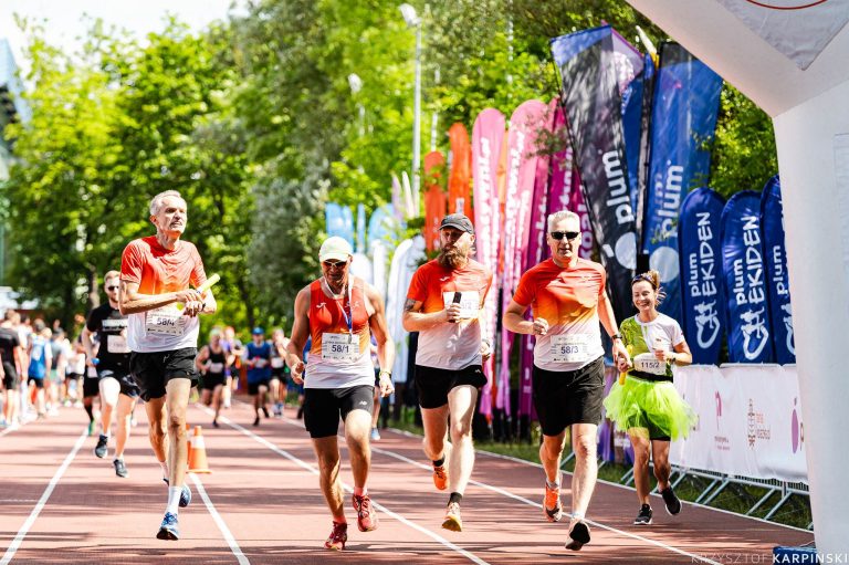 sportowcy biegna w biegu ekiden wsrod zieleni drzew w tle flagi z imprezy