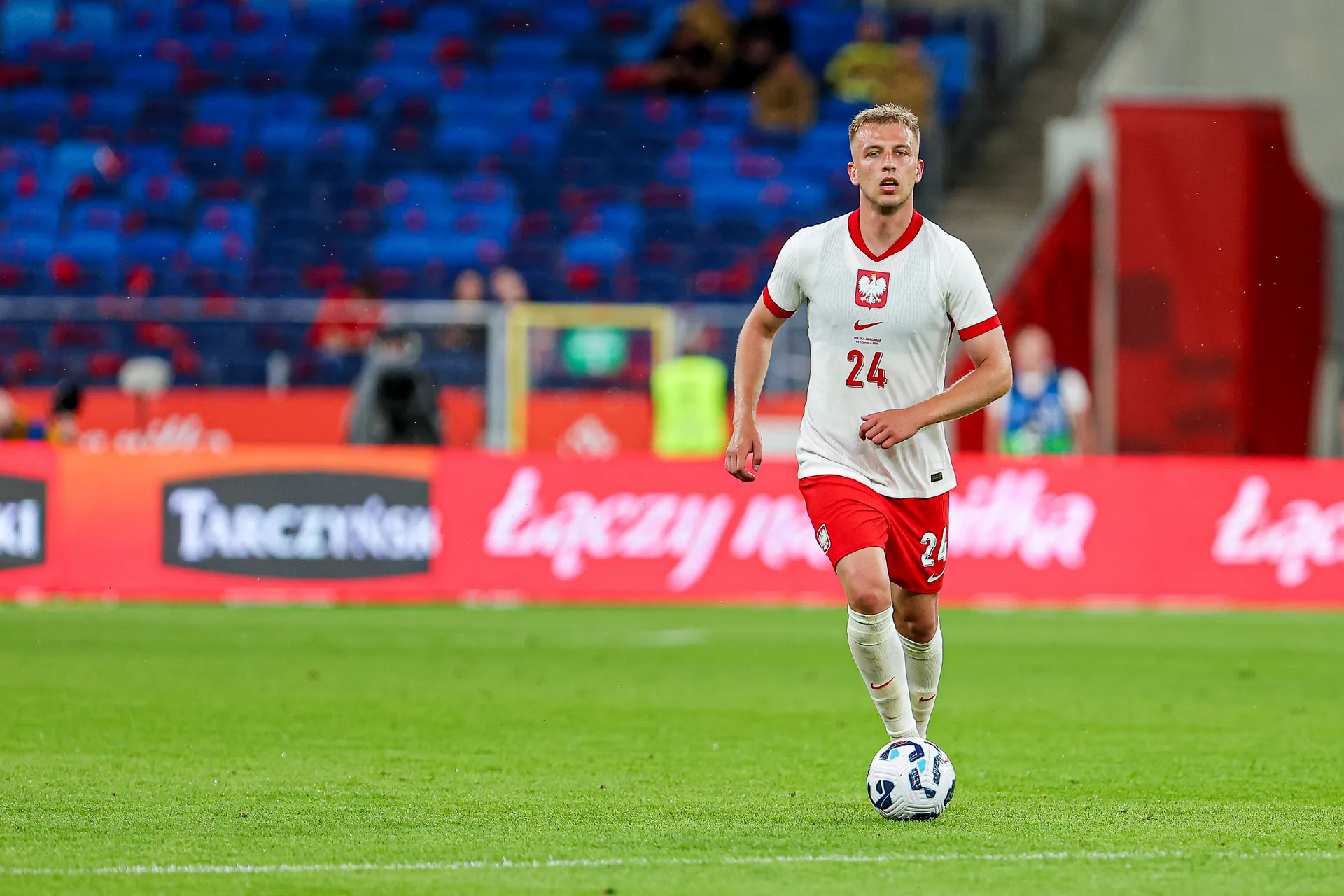 Mateusz Skrzypczak biegnie z piłką po zielonej murawie, nosi białą koszulkę reprezentacji Polski