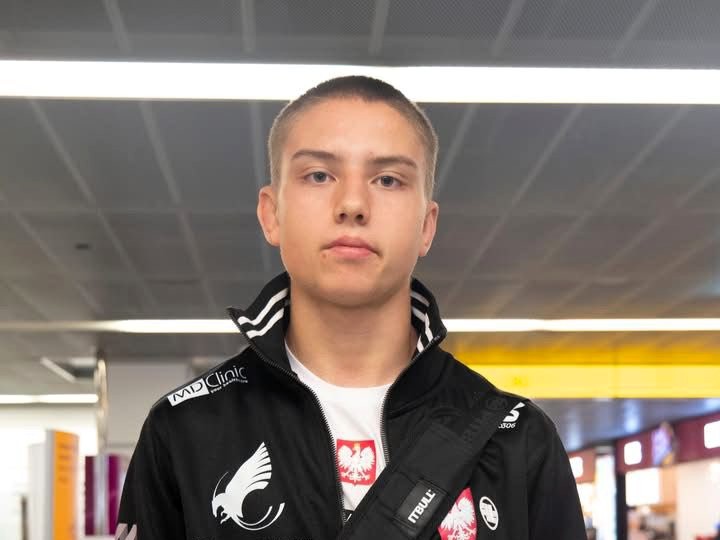 Wojciech Wyszyński w reprezentacyjnym dresie Polski, na tle hali lotniska, przed wylotem na Mistrzostwa Świata Juniorów MMA w Abu Dhabi