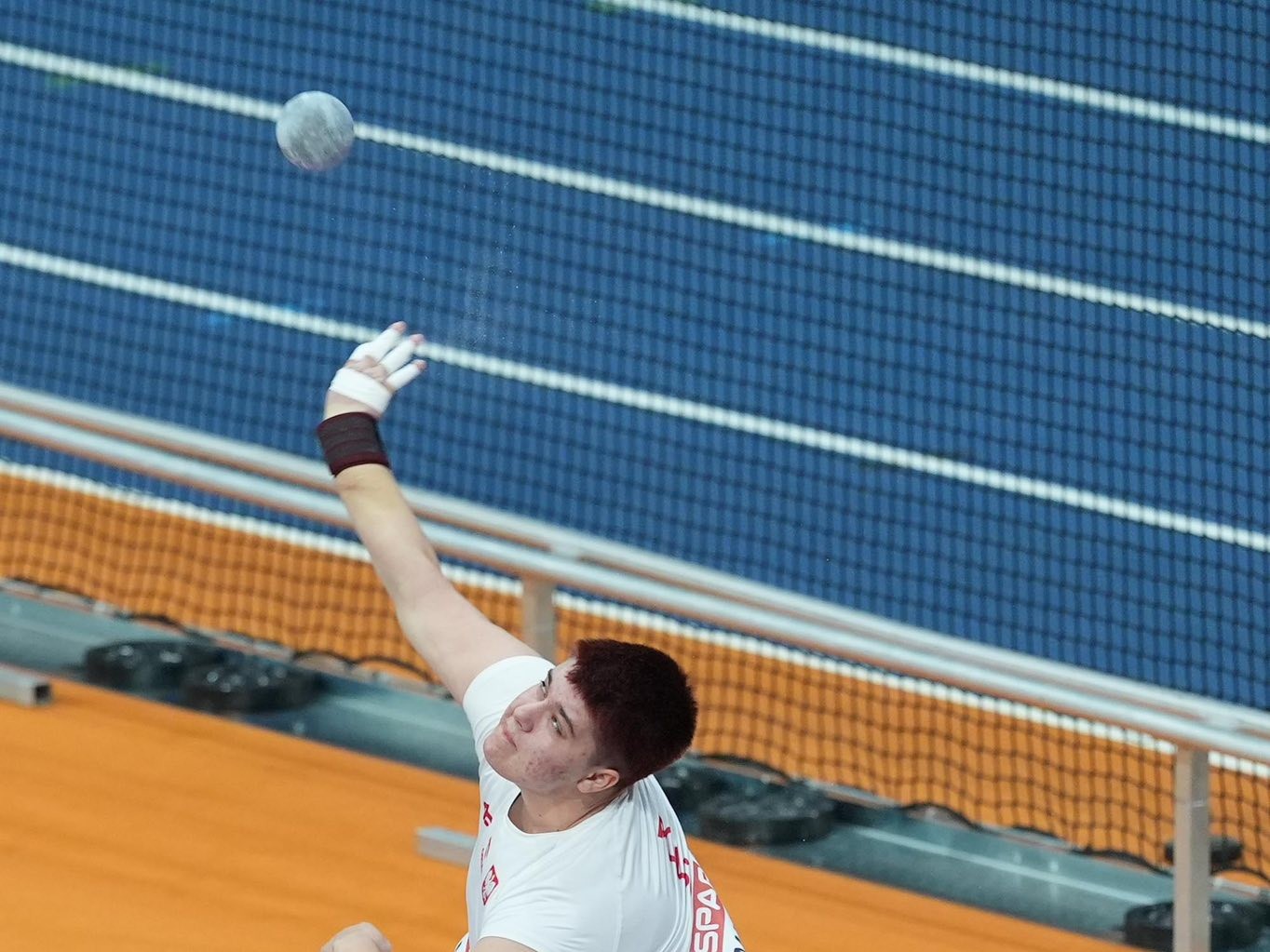 Zuzanna Maślana w biało-czerwonym stroju reprezentacji Polski w trakcie pchnięcia kulą na zawodach lekkoatletycznych.