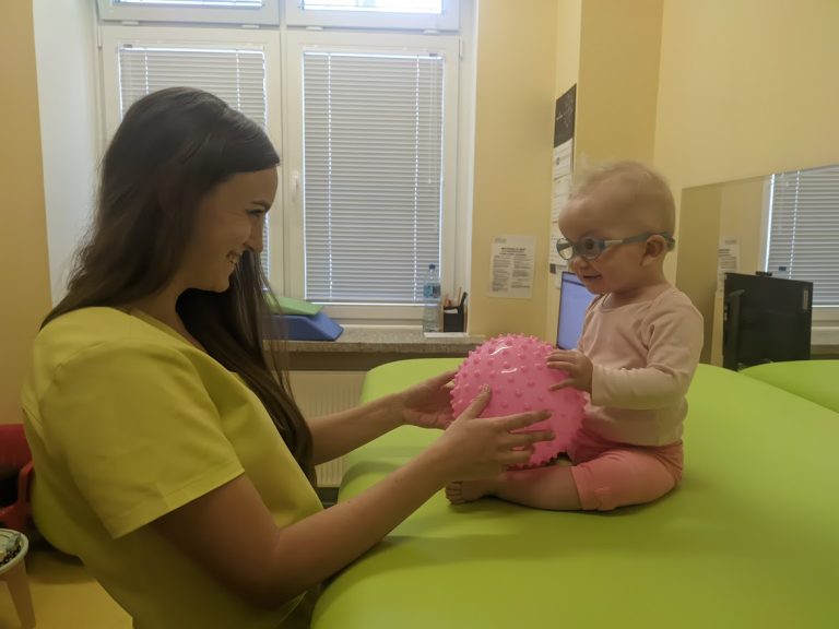 Kobieta trzyma dziecko na stole rehabilitacyjnym.