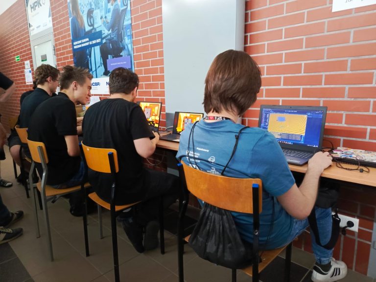 Na zdjęciu widać uczestników konkursu BialJam 2025 organizowanego przez Politechnikę Białostocką. Młodzi twórcy intensywnie pracują nad swoimi grami wideo – projektują grafikę, piszą kod i testują pomysły. Atmosfera skupienia i kreatywności jest wyczuwalna – to właśnie w takich warunkach rodzą się innowacyjne projekty, które mogą stać się początkiem profesjonalnej kariery w branży gier komputerowych.