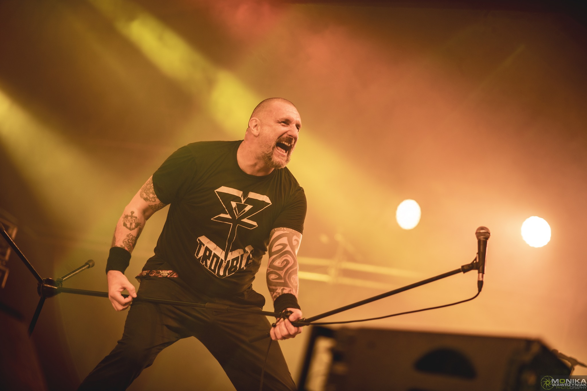 Wokalista zespołu na scenie Summer Dying Loud 2025 w Aleksandrowie Łódzkim – dynamiczny występ w pomarańczowym świetle reflektorów.
