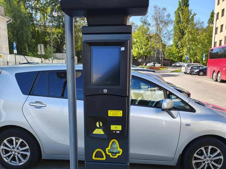 Nowy parkomat w Strefie Płatnego Parkowania w Białymstoku z funkcją płatności kartą i BLIK-iem. W tle zaparkowane samochody na miejskim parkingu.