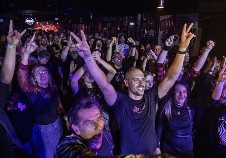 Publiczność w Klubie Sześcian w Białymstoku podczas IX Koncertu Listy Przebojów Kultowej AKADERY, z uniesionymi rękami i entuzjazmem reagująca na występy zespołów rockowych.