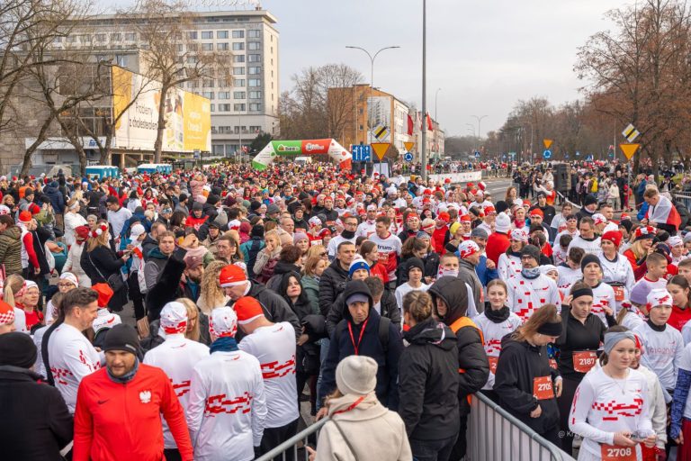 Tłum biegaczy w biało-czerwonych koszulkach i czapkach gromadzi się na starcie przy Alei Piłsudskiego w Białymstoku.